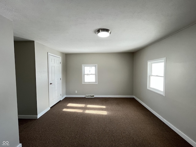 empty room with visible vents, a textured ceiling, baseboards, and dark colored carpet