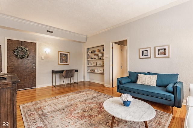 living room featuring a textured ceiling, built in features, crown molding, and hardwood / wood-style floors