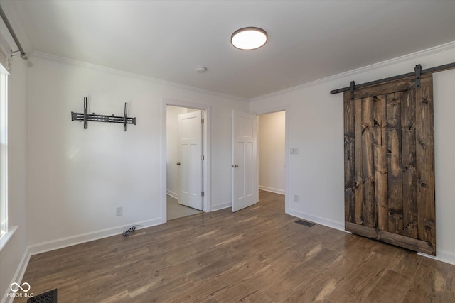 unfurnished bedroom featuring a barn door, dark hardwood / wood-style floors, and crown molding