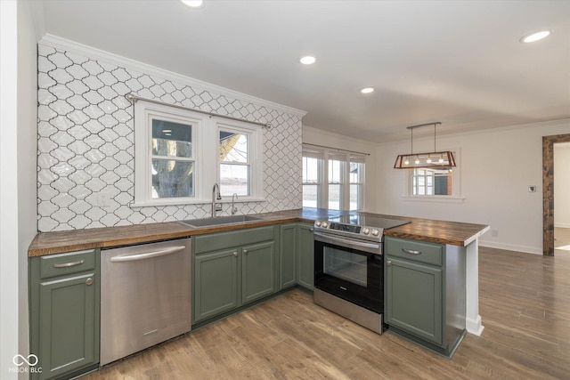 kitchen with wood counters, kitchen peninsula, stainless steel appliances, sink, and decorative light fixtures