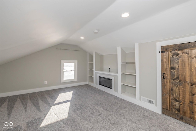 unfurnished living room featuring carpet flooring, built in shelves, and vaulted ceiling