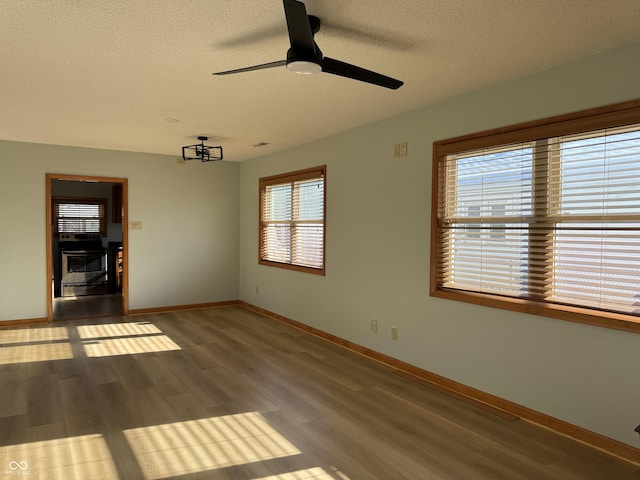 empty room featuring a textured ceiling, hardwood / wood-style flooring, plenty of natural light, and ceiling fan