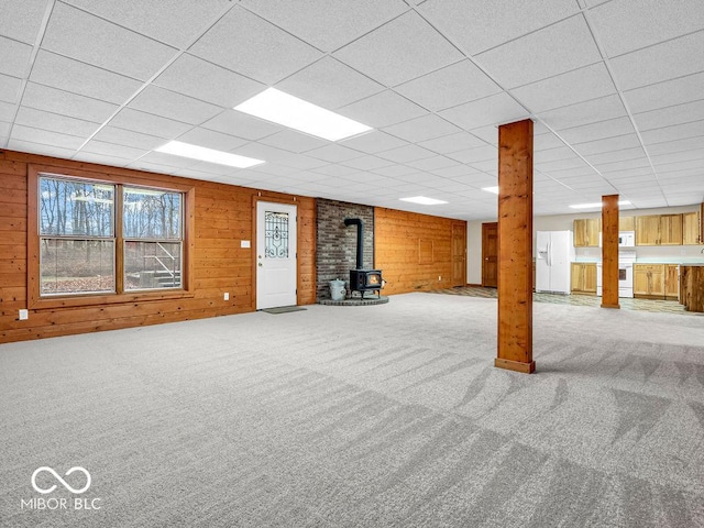 basement with white refrigerator with ice dispenser, carpet floors, a wood stove, and wood walls