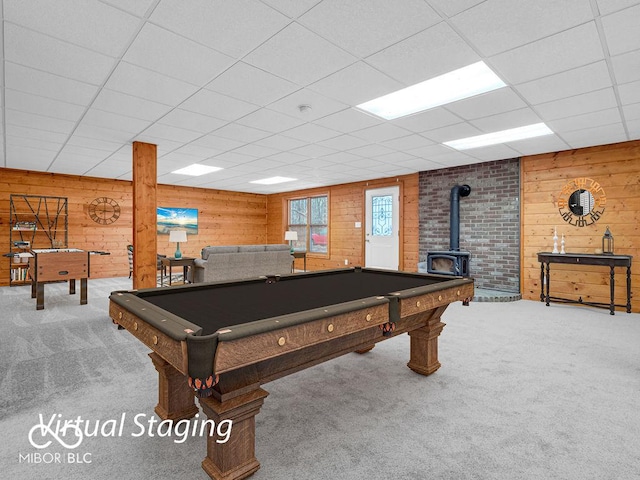 rec room featuring carpet, a drop ceiling, a wood stove, and wooden walls