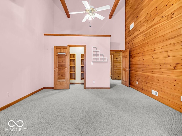 unfurnished living room featuring beamed ceiling, carpet floors, high vaulted ceiling, and wooden walls