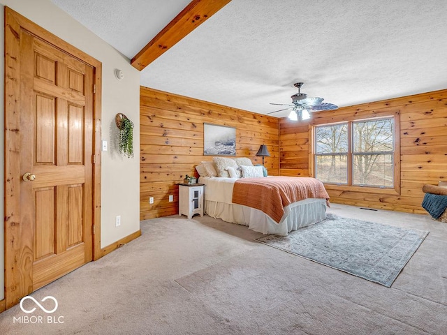 bedroom featuring carpet flooring, a textured ceiling, ceiling fan, wooden walls, and beamed ceiling