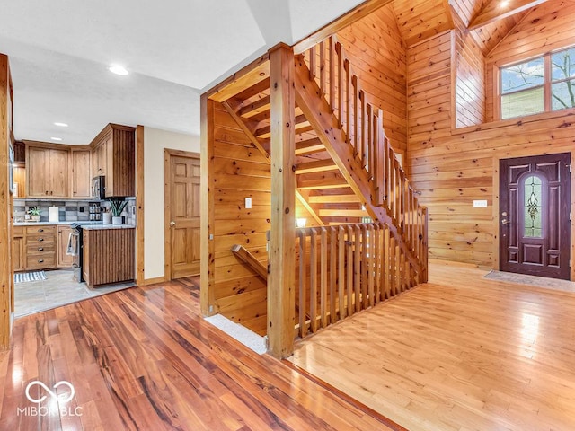 foyer entrance featuring light hardwood / wood-style floors, vaulted ceiling, and wood walls