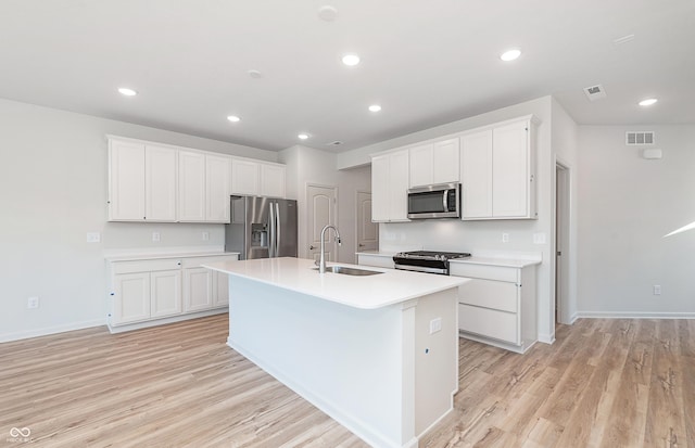 kitchen with white cabinets, stainless steel appliances, a kitchen island with sink, and sink