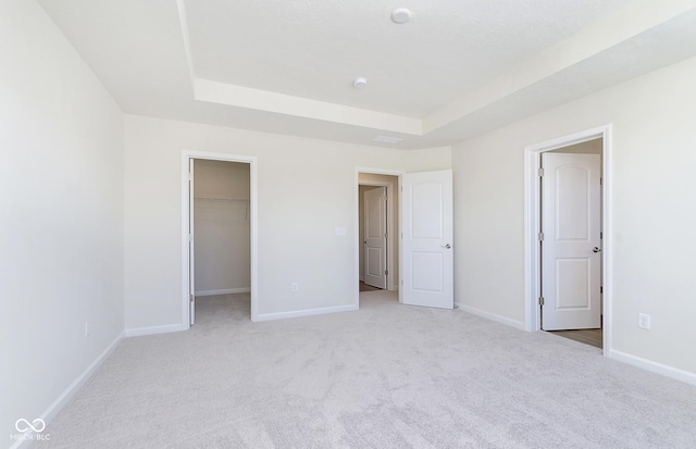 unfurnished bedroom featuring a walk in closet, a raised ceiling, light colored carpet, and a closet