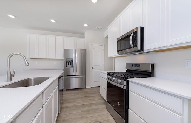 kitchen with sink, stainless steel appliances, white cabinets, and light wood-type flooring