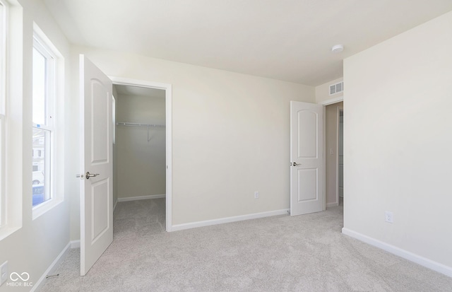 unfurnished bedroom with a spacious closet, light colored carpet, and a closet