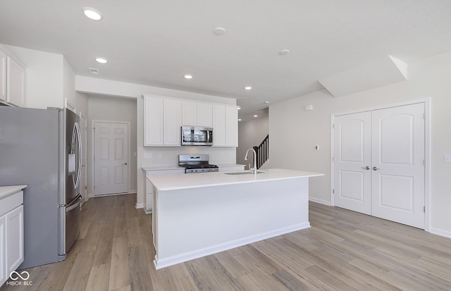 kitchen with sink, appliances with stainless steel finishes, light hardwood / wood-style floors, white cabinets, and a center island with sink