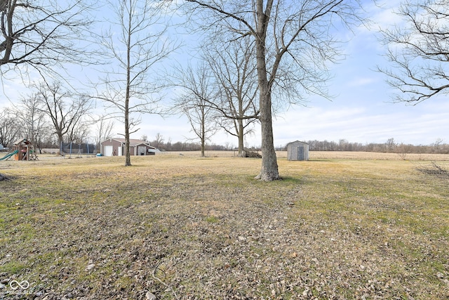 view of yard featuring a rural view, a storage shed, and a playground