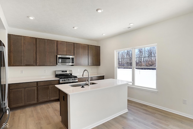 kitchen with dark brown cabinetry, sink, light hardwood / wood-style flooring, a center island with sink, and appliances with stainless steel finishes