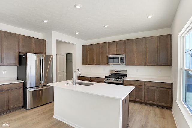 kitchen with a center island with sink, light wood-type flooring, sink, and appliances with stainless steel finishes