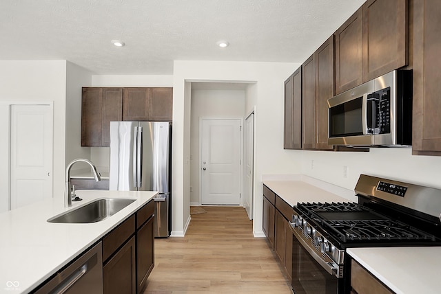 kitchen featuring appliances with stainless steel finishes, light wood-type flooring, dark brown cabinetry, a textured ceiling, and sink