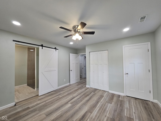 unfurnished bedroom with ceiling fan, light hardwood / wood-style flooring, a barn door, and multiple closets