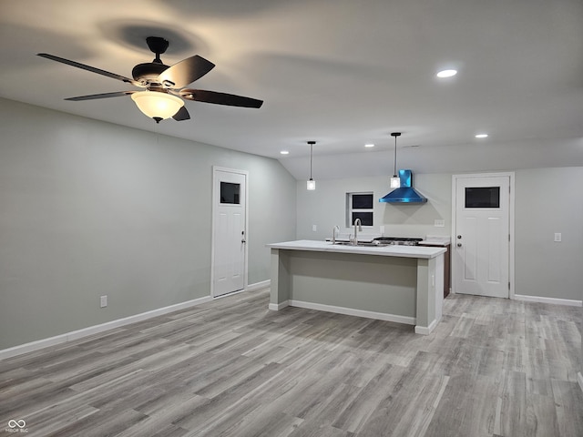 kitchen featuring pendant lighting, wall chimney exhaust hood, sink, light wood-type flooring, and a center island with sink