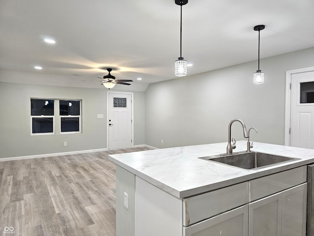 kitchen with sink, hanging light fixtures, a center island with sink, and light hardwood / wood-style flooring