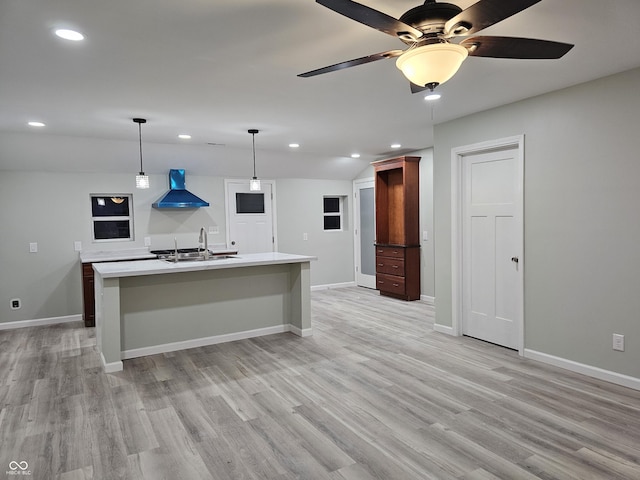 kitchen featuring a center island with sink, pendant lighting, wall chimney exhaust hood, light hardwood / wood-style flooring, and sink