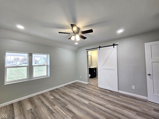 unfurnished bedroom with connected bathroom, ceiling fan, a barn door, and hardwood / wood-style flooring