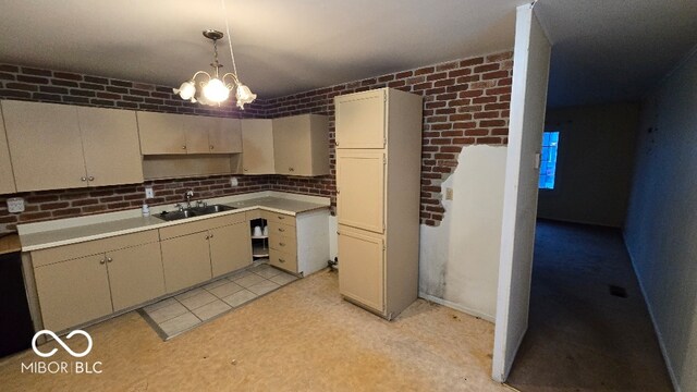 kitchen with cream cabinetry, hanging light fixtures, brick wall, and an inviting chandelier