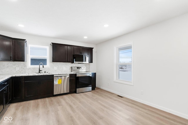 kitchen featuring dark brown cabinets, light stone counters, light wood-type flooring, and appliances with stainless steel finishes