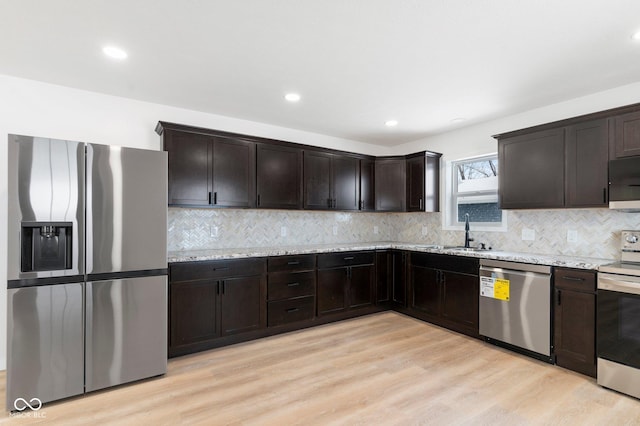 kitchen with appliances with stainless steel finishes, light hardwood / wood-style floors, light stone counters, and sink