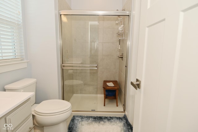 bathroom featuring a shower with door, vanity, and toilet