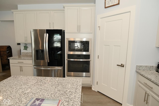 kitchen featuring light stone countertops, stainless steel refrigerator with ice dispenser, double oven, built in microwave, and light hardwood / wood-style flooring