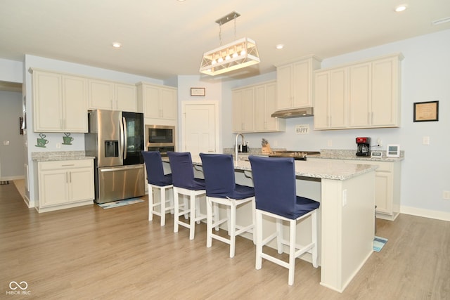 kitchen featuring hanging light fixtures, light hardwood / wood-style flooring, an island with sink, appliances with stainless steel finishes, and light stone counters