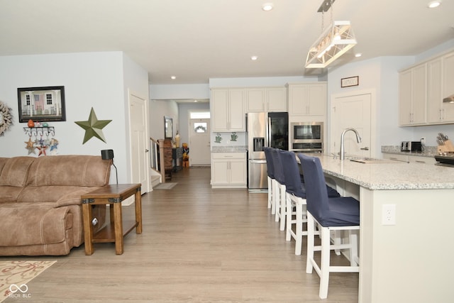 kitchen with built in microwave, stainless steel fridge with ice dispenser, light hardwood / wood-style flooring, decorative light fixtures, and a breakfast bar