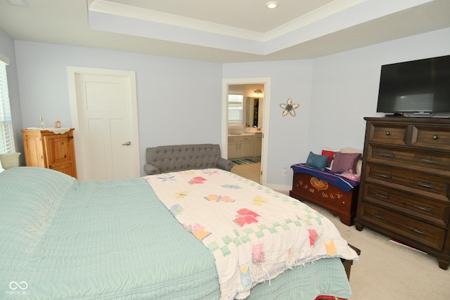 bedroom with a raised ceiling, ensuite bathroom, and light colored carpet