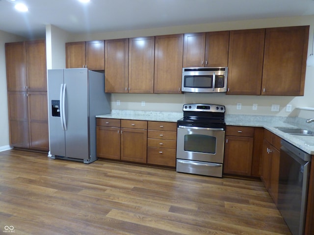 kitchen with light stone counters, sink, wood-type flooring, and appliances with stainless steel finishes