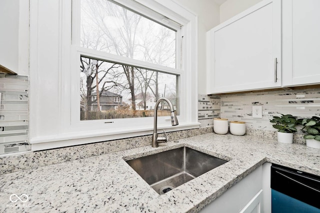 kitchen featuring decorative backsplash, light stone countertops, sink, white cabinets, and black dishwasher