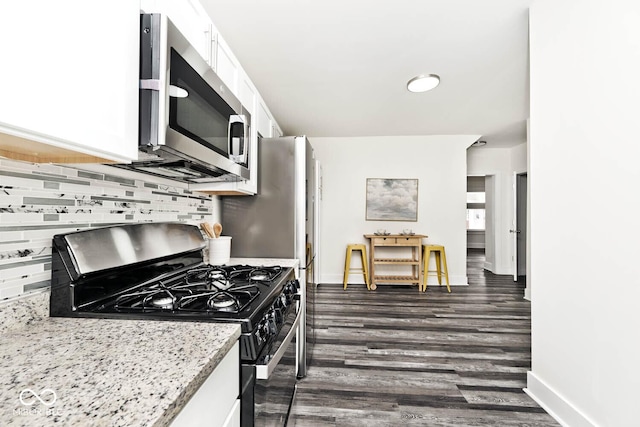 kitchen with dark wood-type flooring, white cabinets, light stone countertops, appliances with stainless steel finishes, and tasteful backsplash