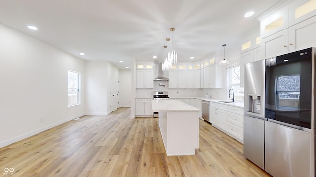 kitchen with wall chimney exhaust hood, a center island, white cabinetry, appliances with stainless steel finishes, and sink