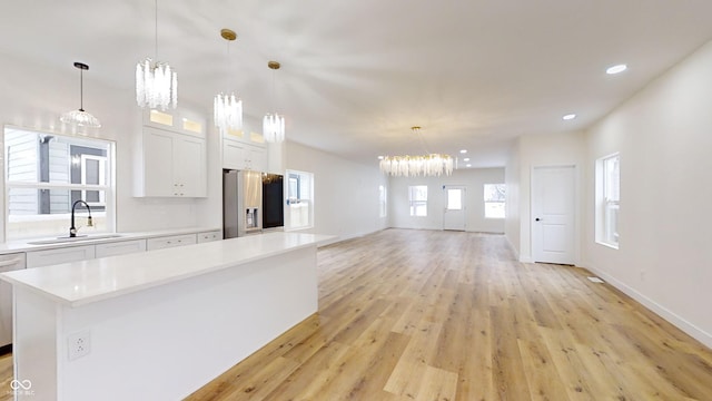 kitchen featuring decorative light fixtures, light hardwood / wood-style floors, white cabinets, appliances with stainless steel finishes, and sink