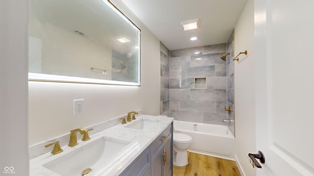 full bathroom featuring hardwood / wood-style floors, tiled shower / bath combo, vanity, and toilet