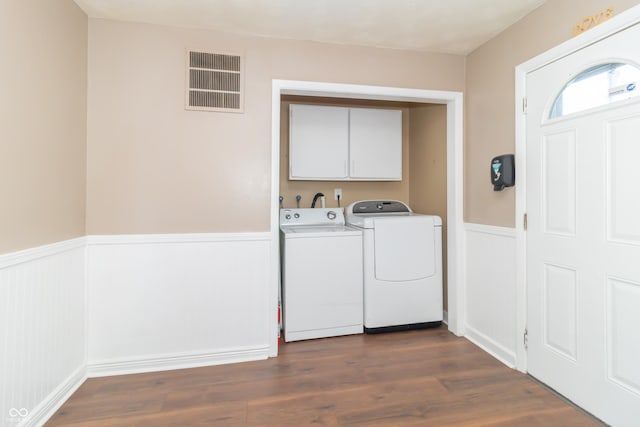 laundry room with dark wood-type flooring, washing machine and clothes dryer, and cabinets