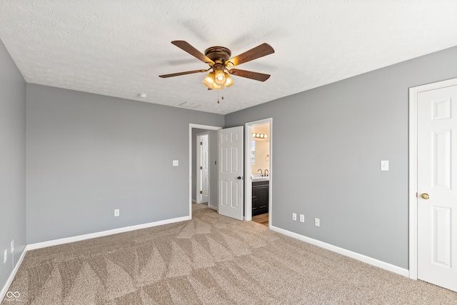 unfurnished bedroom featuring ensuite bathroom, sink, ceiling fan, light carpet, and a textured ceiling