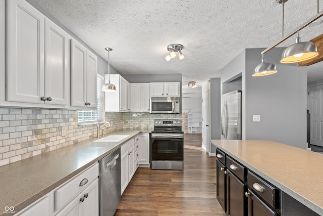 kitchen featuring sink, hanging light fixtures, stainless steel appliances, decorative backsplash, and white cabinets