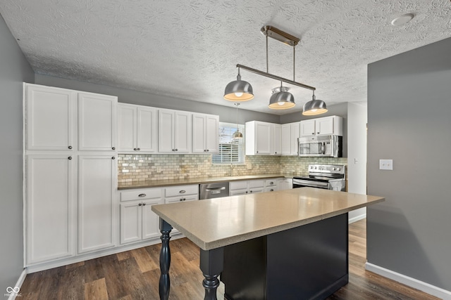 kitchen with pendant lighting, appliances with stainless steel finishes, white cabinetry, a center island, and dark hardwood / wood-style flooring