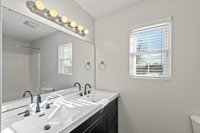 bathroom featuring vanity, a textured ceiling, a shower, and toilet