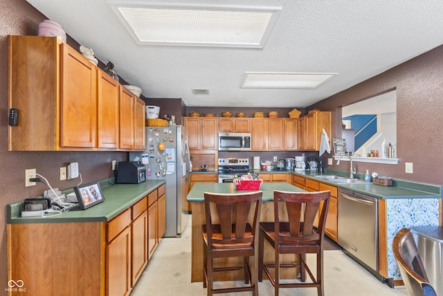 kitchen featuring stainless steel appliances, sink, a textured ceiling, a kitchen bar, and a kitchen island