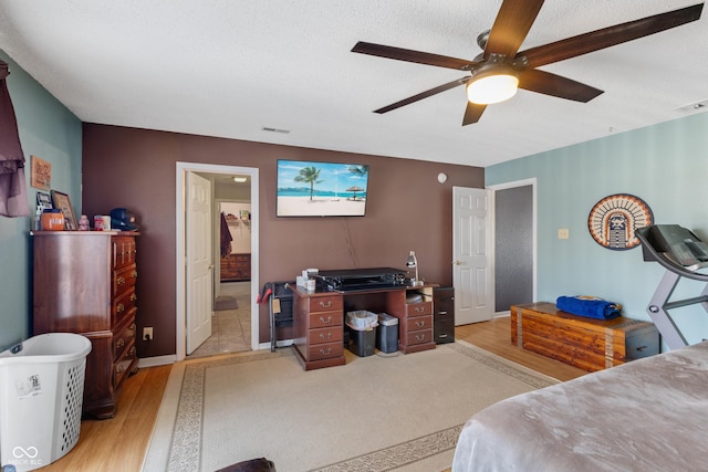 bedroom with ceiling fan, light hardwood / wood-style flooring, ensuite bathroom, and a textured ceiling