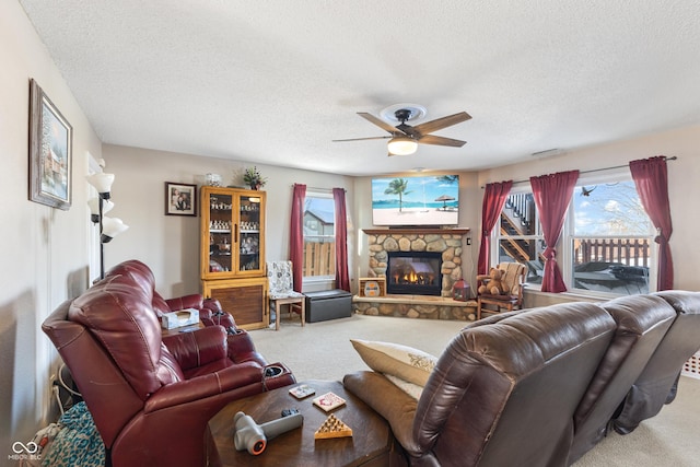 carpeted living room featuring a textured ceiling, ceiling fan, and a stone fireplace