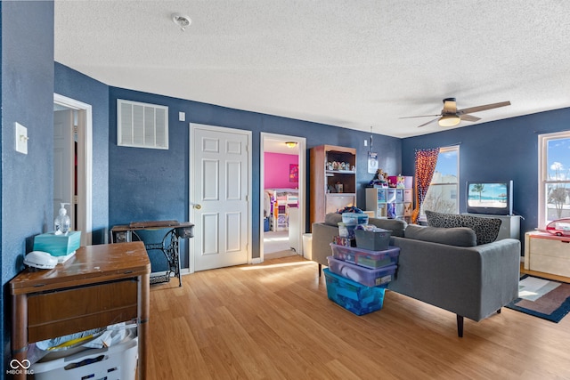 living room with a textured ceiling, ceiling fan, and light wood-type flooring