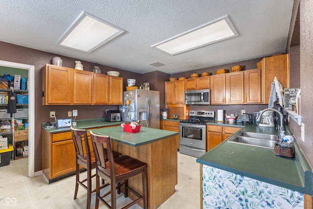 kitchen featuring stainless steel appliances, sink, a textured ceiling, a kitchen bar, and a kitchen island