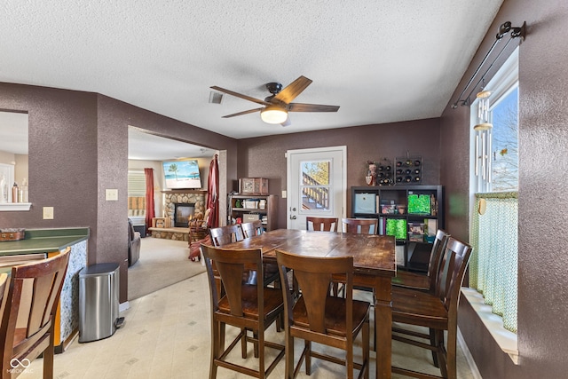 dining room featuring a textured ceiling, ceiling fan, and a stone fireplace